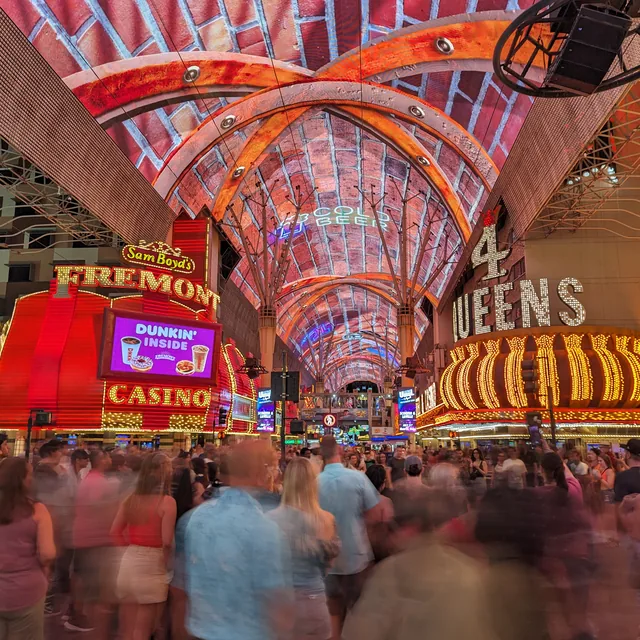 Fremont Street in Las Vegas at night: the Fremont and 4 Queens casino signs blazing under the LED canopy, crowds below.